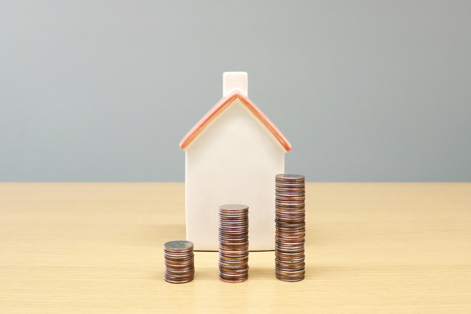 Maqueta de una casa junto a pilas de monedas, ilustrando el valor del metro cuadrado